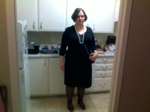 A picture of me heading out for a swankier evening. I'm wearing a knee-length, black wrap dress with a low v-neck, three-quarter sleeves and ruching through the torso. The lace part of a black camisole is showing above the v-neck to prevent clevage. A long strand of cream pearls is lying over the dress and falling just below my bust. A black quilted cross-body bag with a silver chain is slung across my body, and I'm wearing black hose and red pumps. I've put on my evening makeup, consisting of slightly deeper blush, a touch of beige eye shadow and dark red lipstick.   